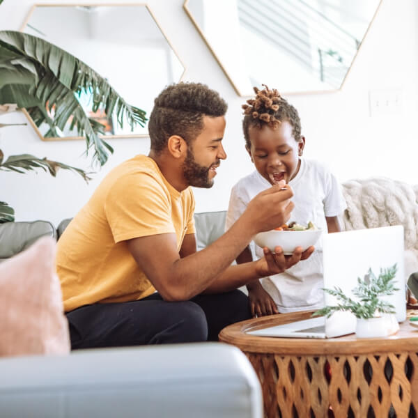 father and sun at home in living room sharing a bowl of cereal